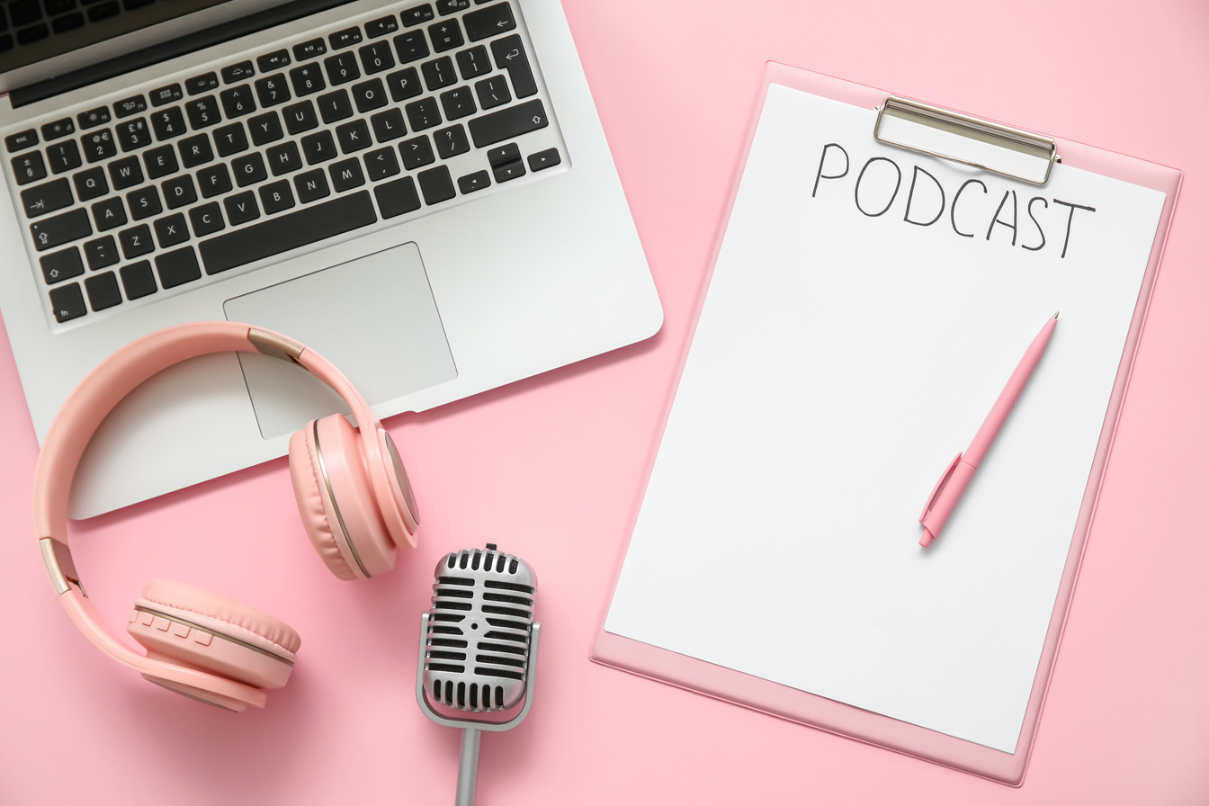 Clipboard with Word PODCAST, Headphones, Microphone and Laptop on Pink Background